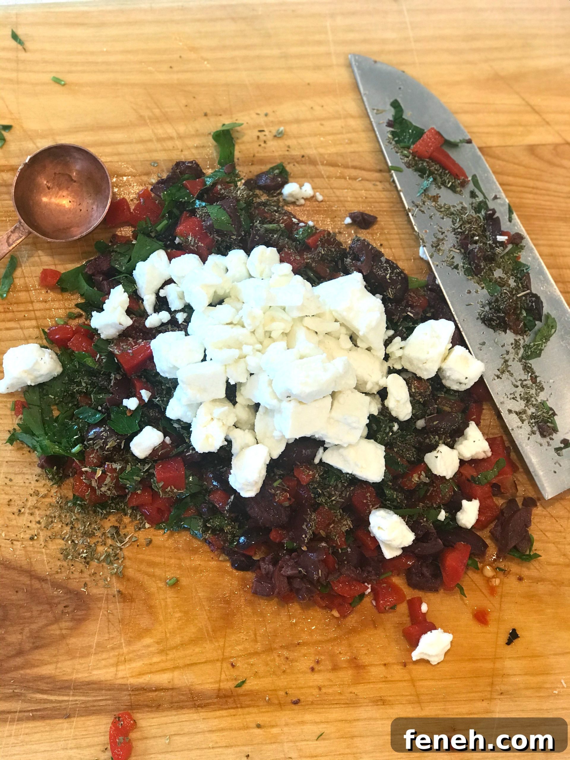 Feta atop a pile of diced ingredients on a cutting board with a knife.