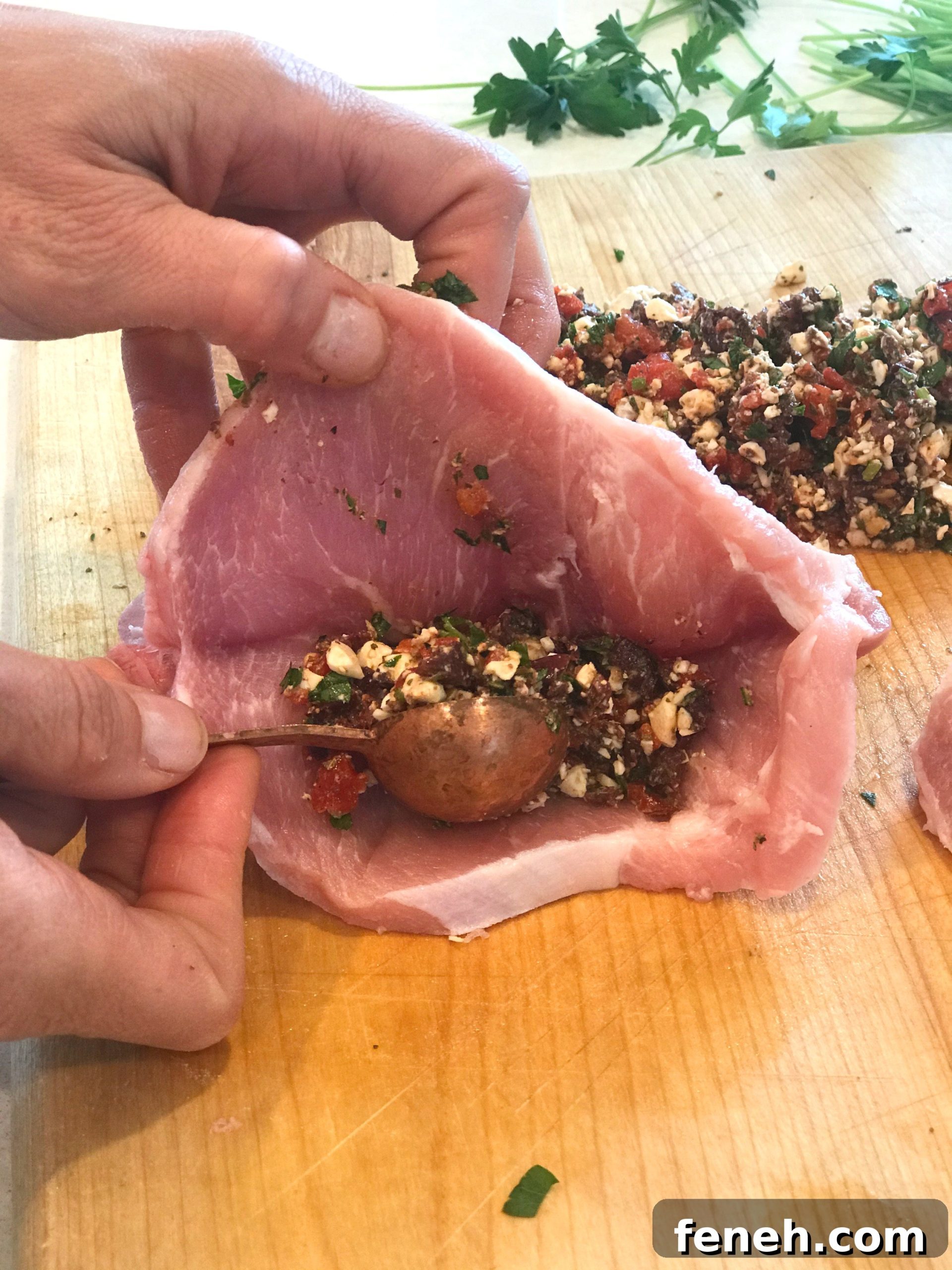 Spoon adding feta filling to a sliced pork chop.