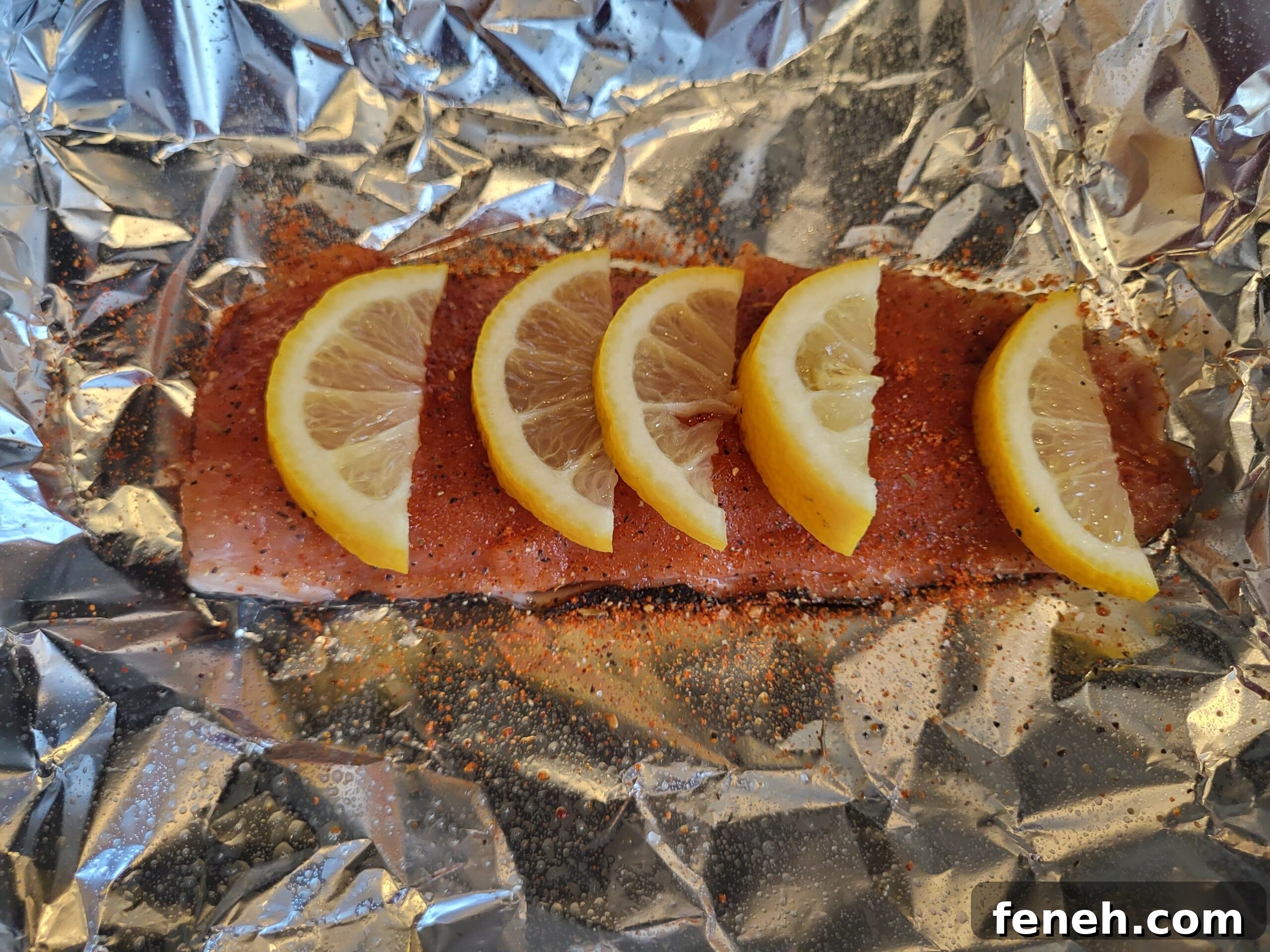 Salmon fillet on foil seasoned with lemon wedges