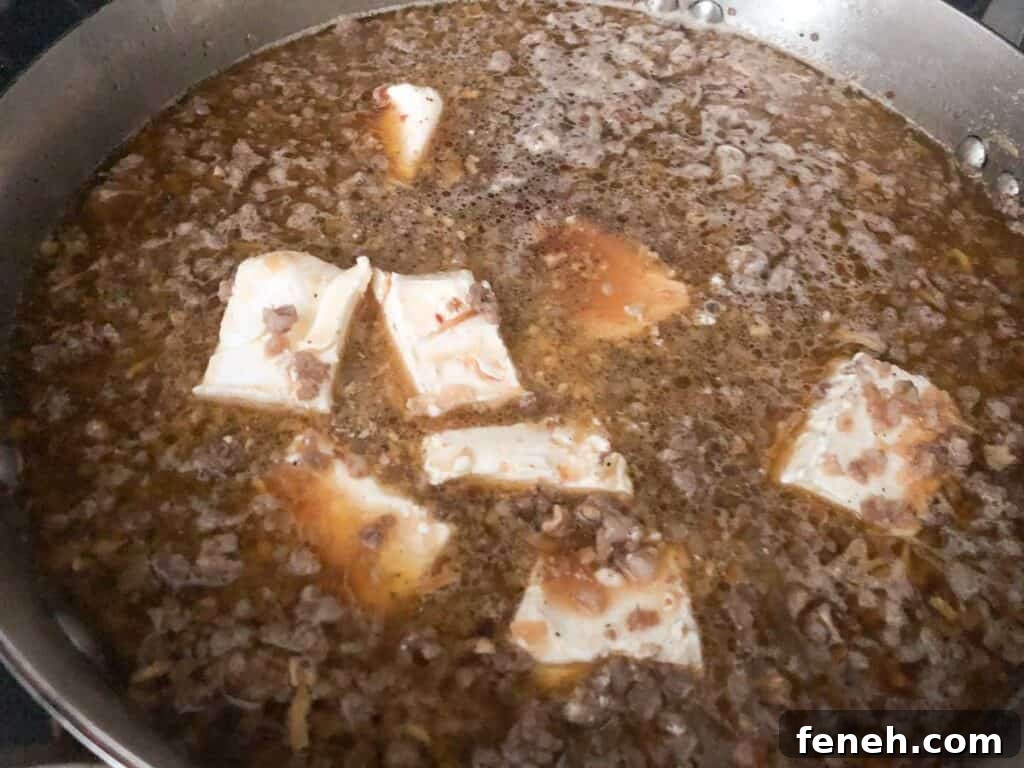 ground sausage with broth and chunks of cream cheese in pan