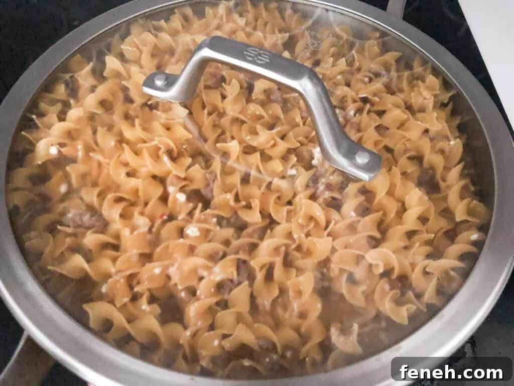creamy sausage pasta cooking in covered pan