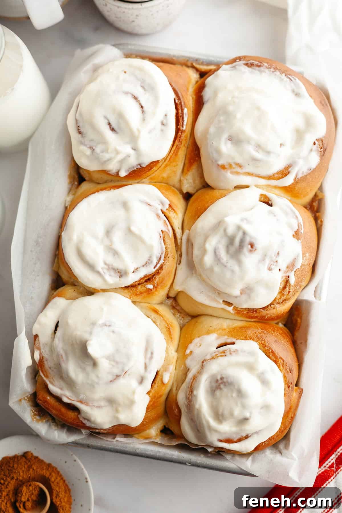 Six cinnamon buns covered in cream cheese icing in a small pan.