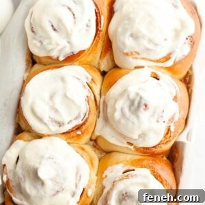 A close up of six cinnamon rolls covered with cream cheese icing.