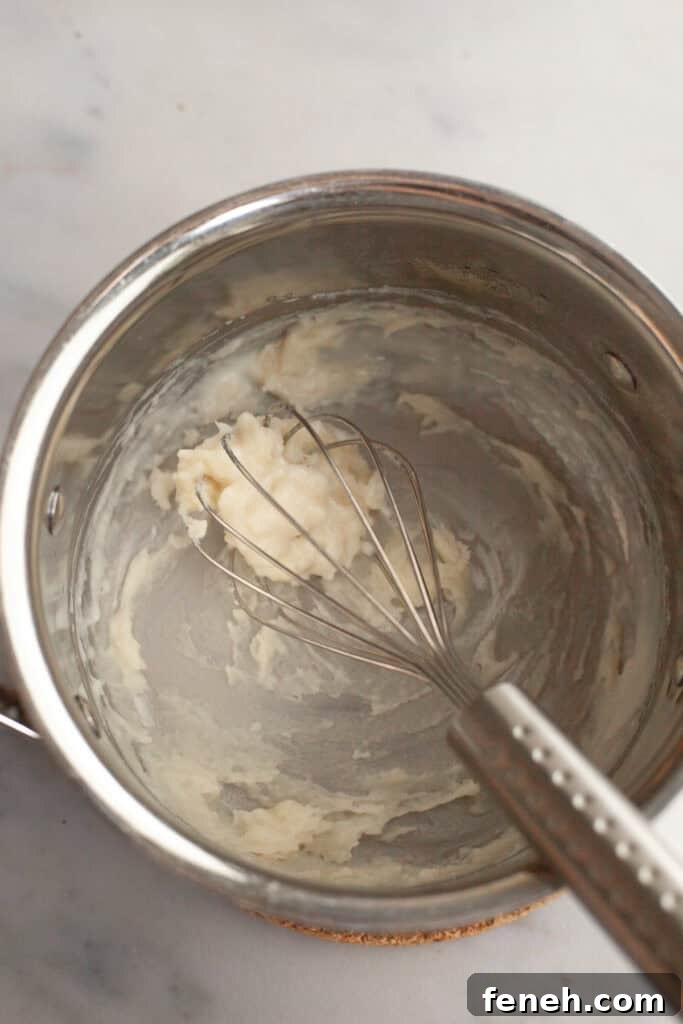 A small silver saucepan with a whisk and tangzhong batter in it.