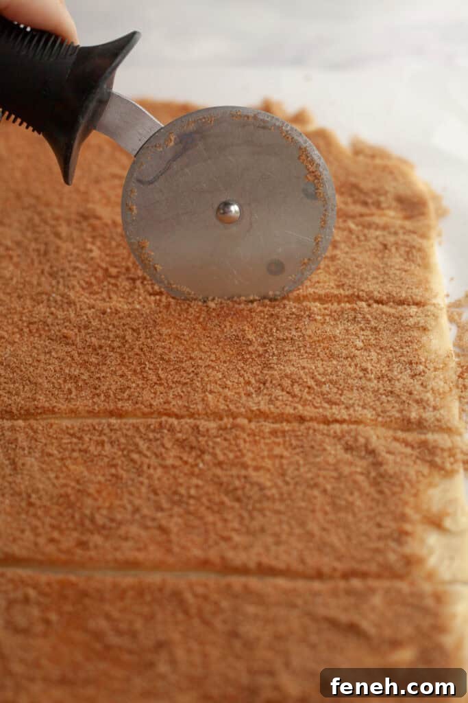 A pizza cutter slicing cinnamon roll dough into strips.