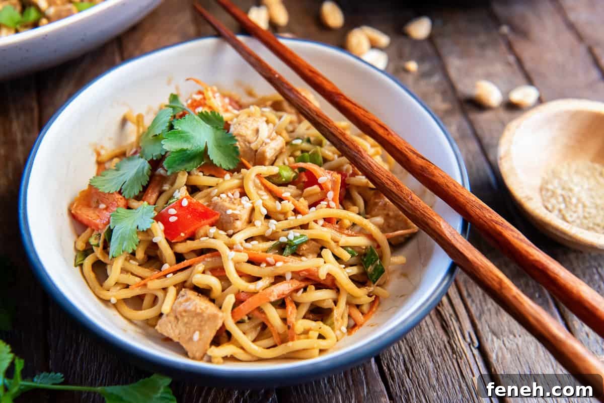 Chopsticks resting on a small bowl filled with peanut noodles with chicken.