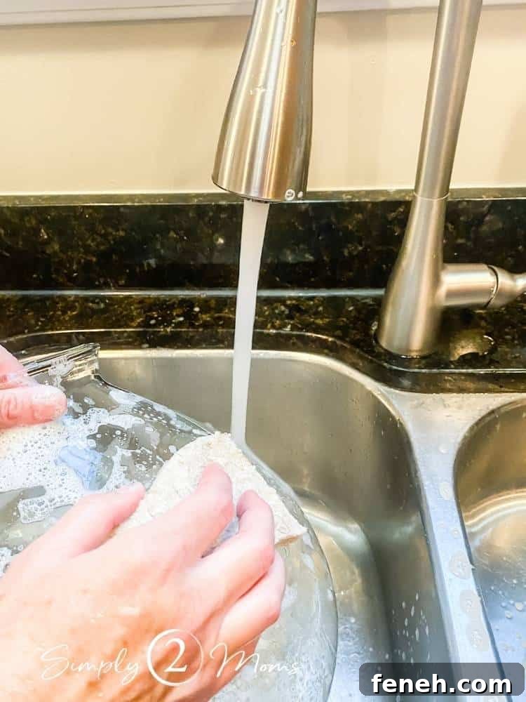 washing glass pendant in kitchen sink with dish soap and sponge under running faucet