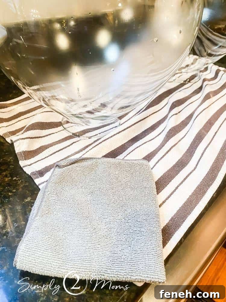 glass globe of light fixture sitting on towel on kitchen counter after washing with microfiber cloth next to it