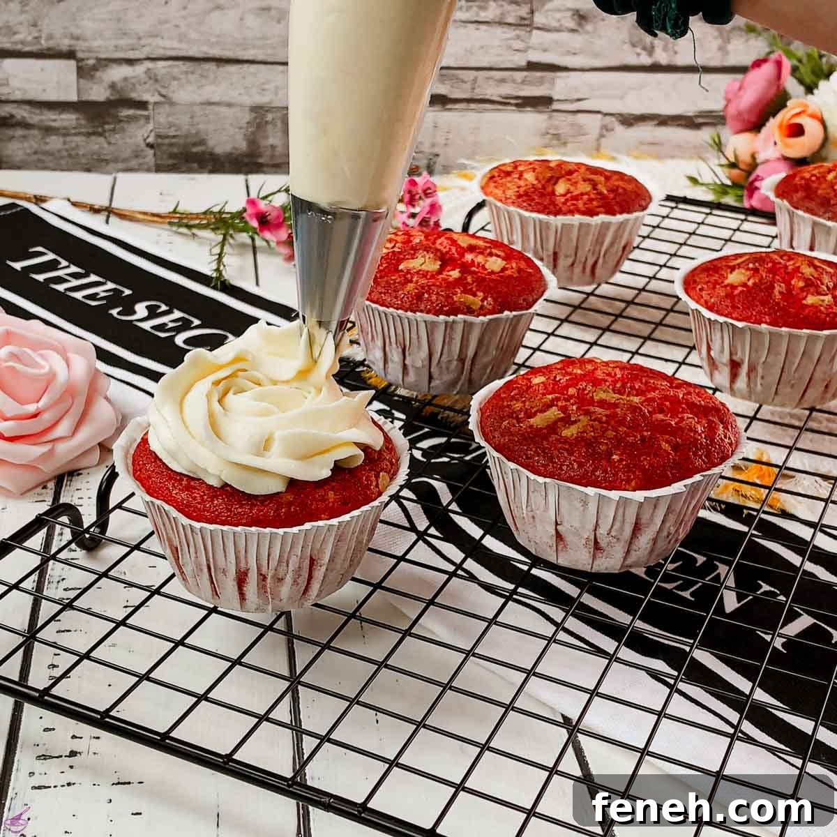 Piping cream cheese frosting on top of red velvet muffin.