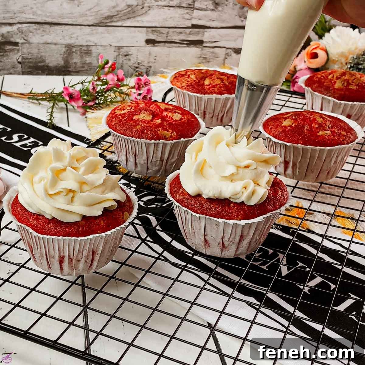Piping cream cheese frosting on top of red velvet muffin.