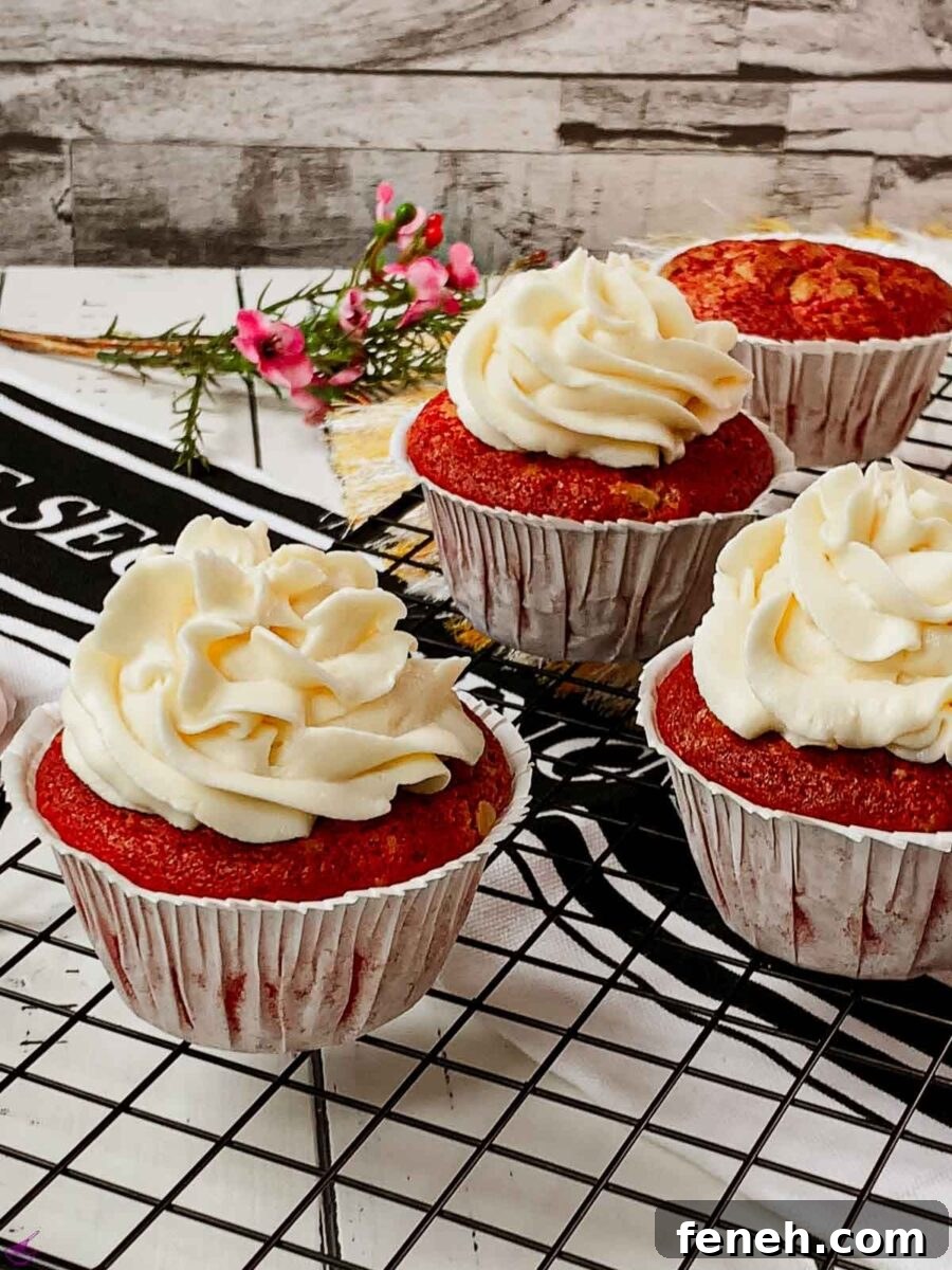 Cream cheese frosting on top of red velvet muffin placed on cooling rack.