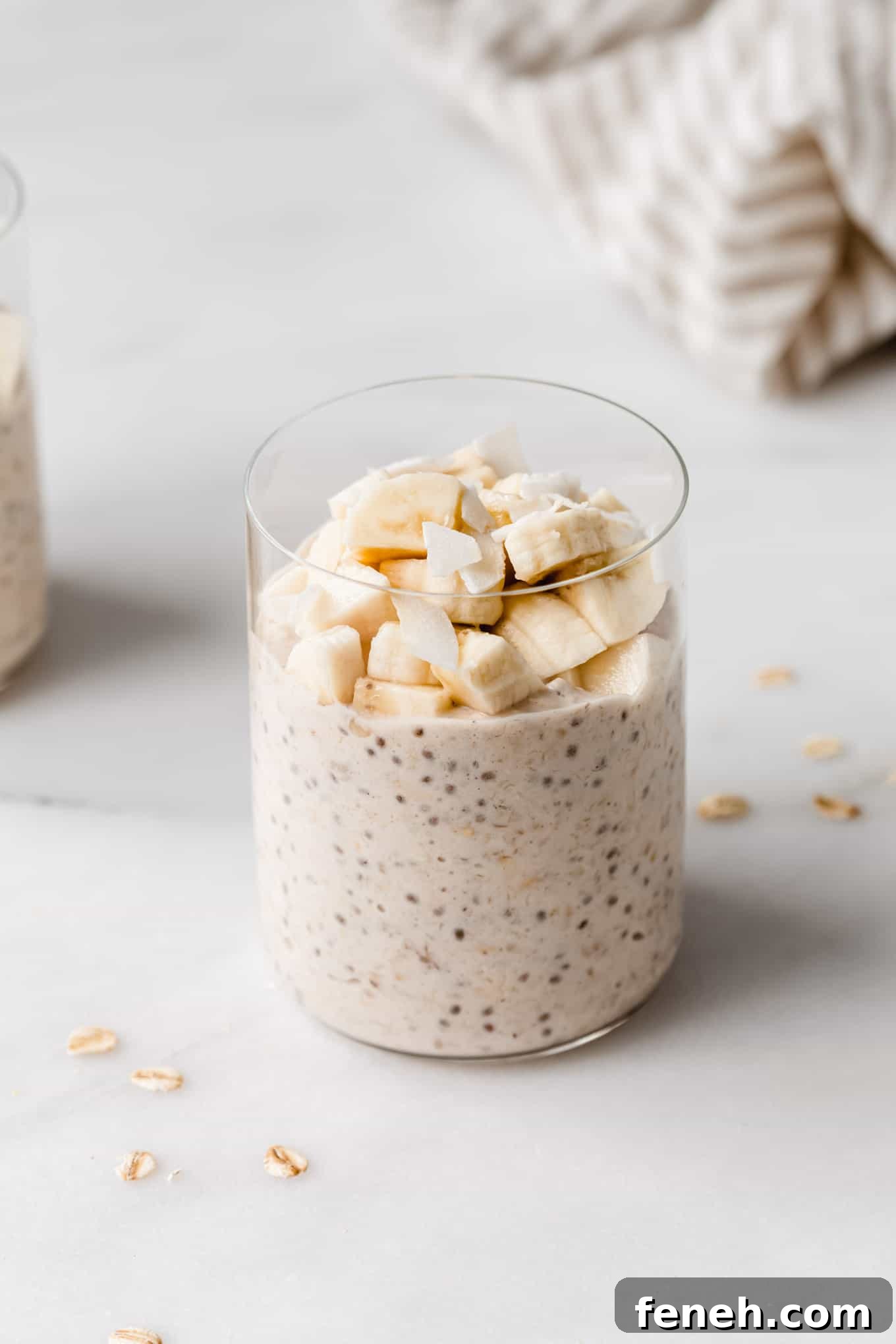 a glass of banana overnight oats topped with banana and coconut flakes.