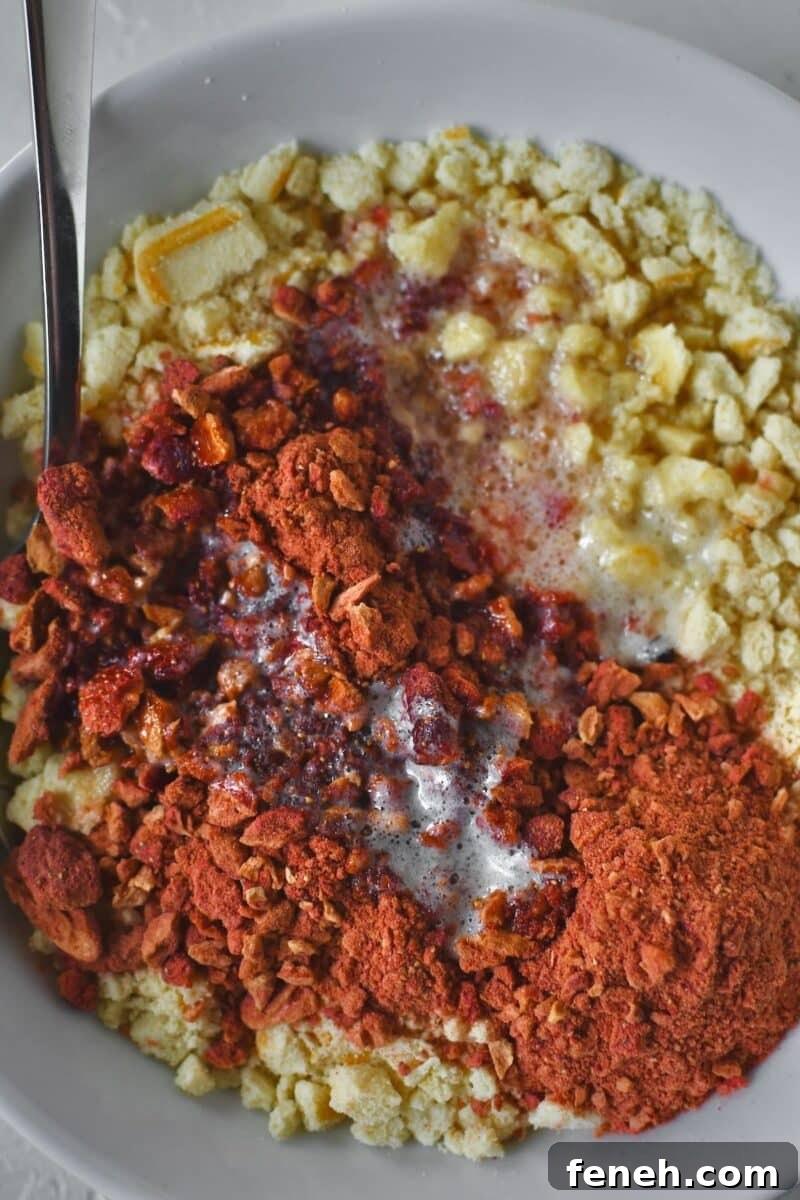 Crushed butter cookies and freeze dried strawberries in a bowl with butter added, before mixing together.