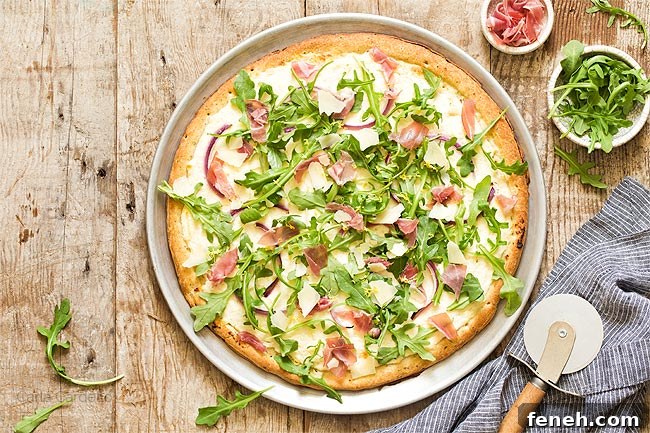 Prosciutto Arugula Pizza on a pizza pan with pizza cutter
