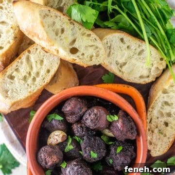 overhead shot of chorizo al vino in orange bowl with slices of bread on wood board