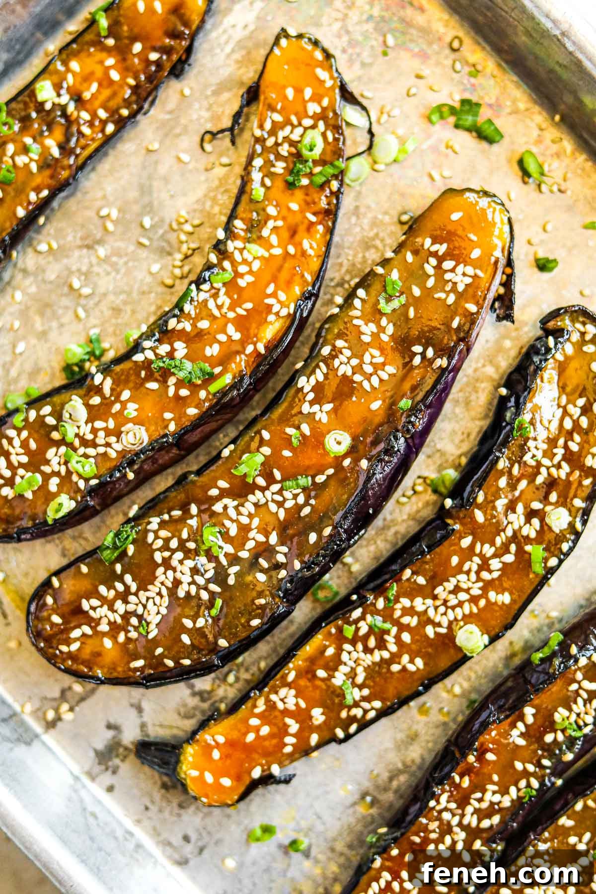 Miso-glazed Japanese eggplant with sesame seeds and sliced green onions on a baking sheet.