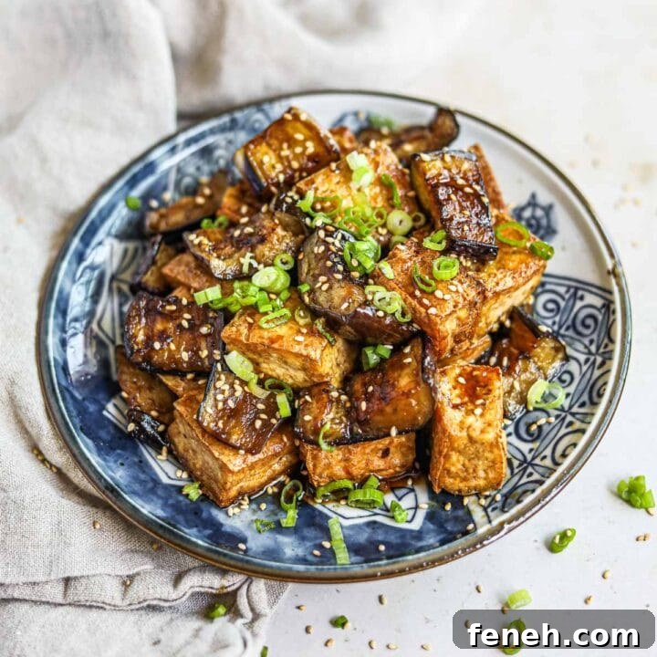Teriyaki fried tofu and Japanese eggplant in a homemade gluten-free honey teriyaki sauce topped with sliced green onions and sesame seeds on a blue plate.