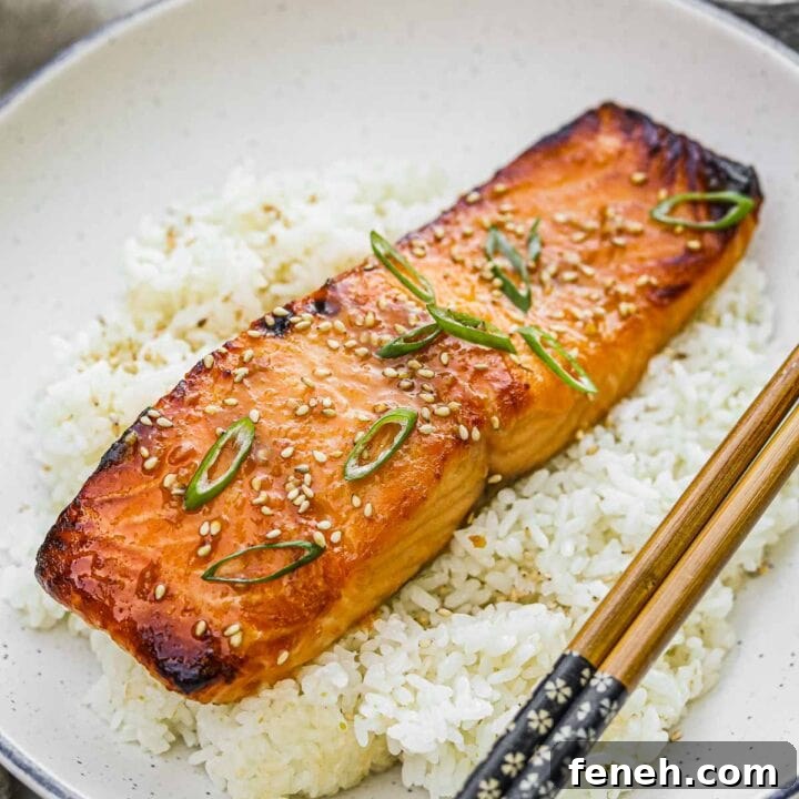 Broiled miso-glazed salmon on a bed of Japanese rice topped with toasted sesame seeds and scallions and served with chopsticks.