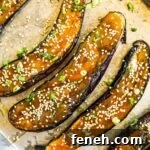 Miso-glazed Japanese eggplant with sesame seeds and sliced green onions on a baking sheet.