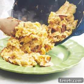 Wooden spatula pushing Matzoh Brei from a skillet to a plate.