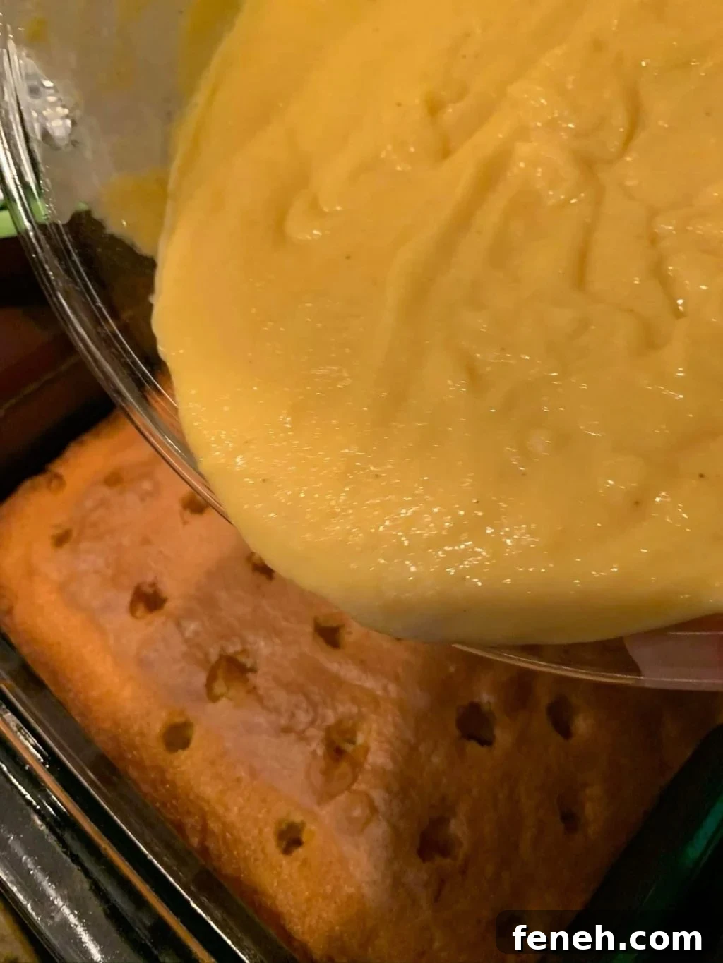 Egg nog pudding being poured from a glass bowl on to a cake with holes poked in it