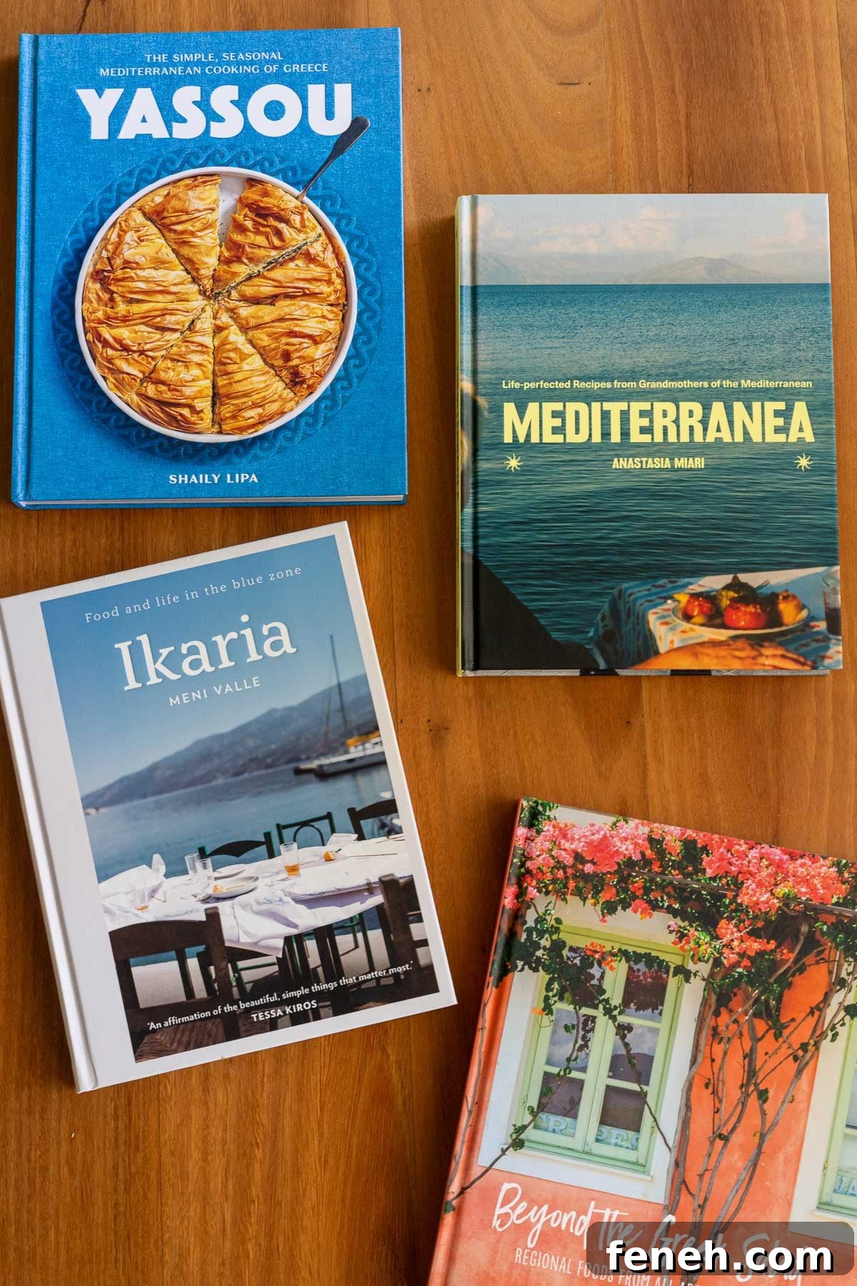 A display of four Greek cookbooks on a wooden table, cover side up.