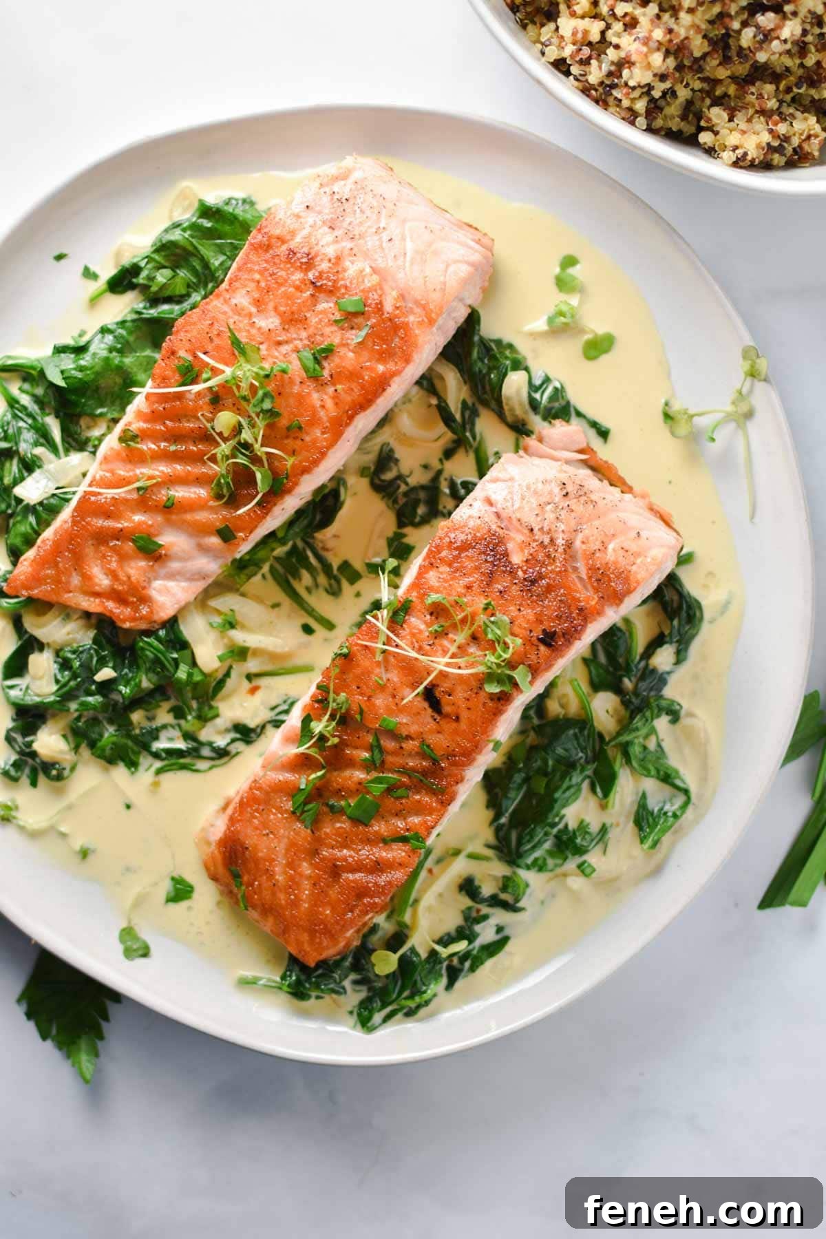 Two filets of salmon on top of spinach surrounded by a creamy sauce next to a bowl of quinoa.