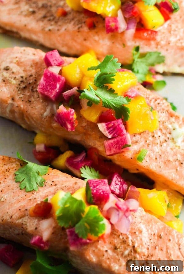Three filets of grilled salmon topped with a mango salsa on a grey plate