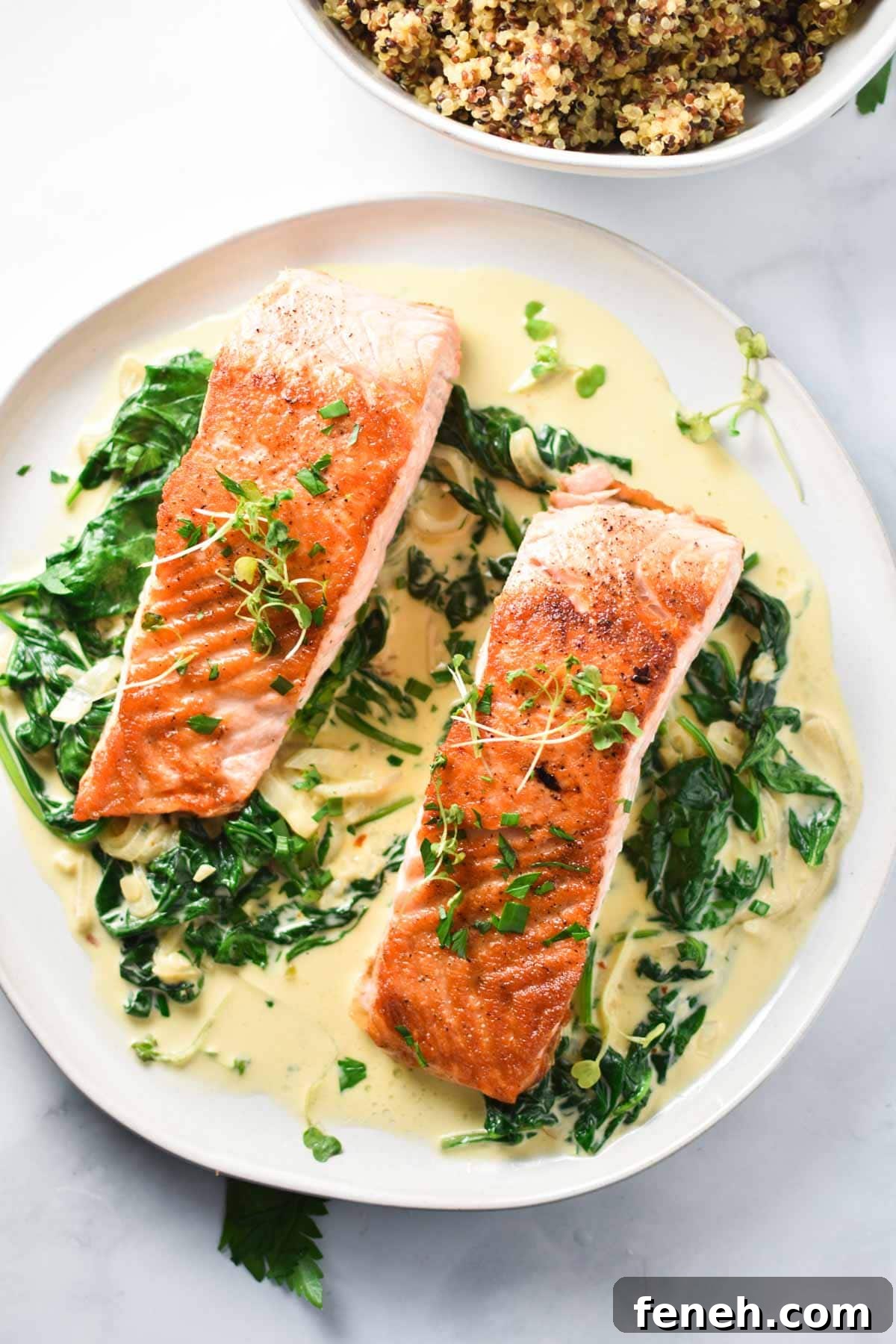 Pan seared salmon on a white plate with creamy spinach and quinoa.