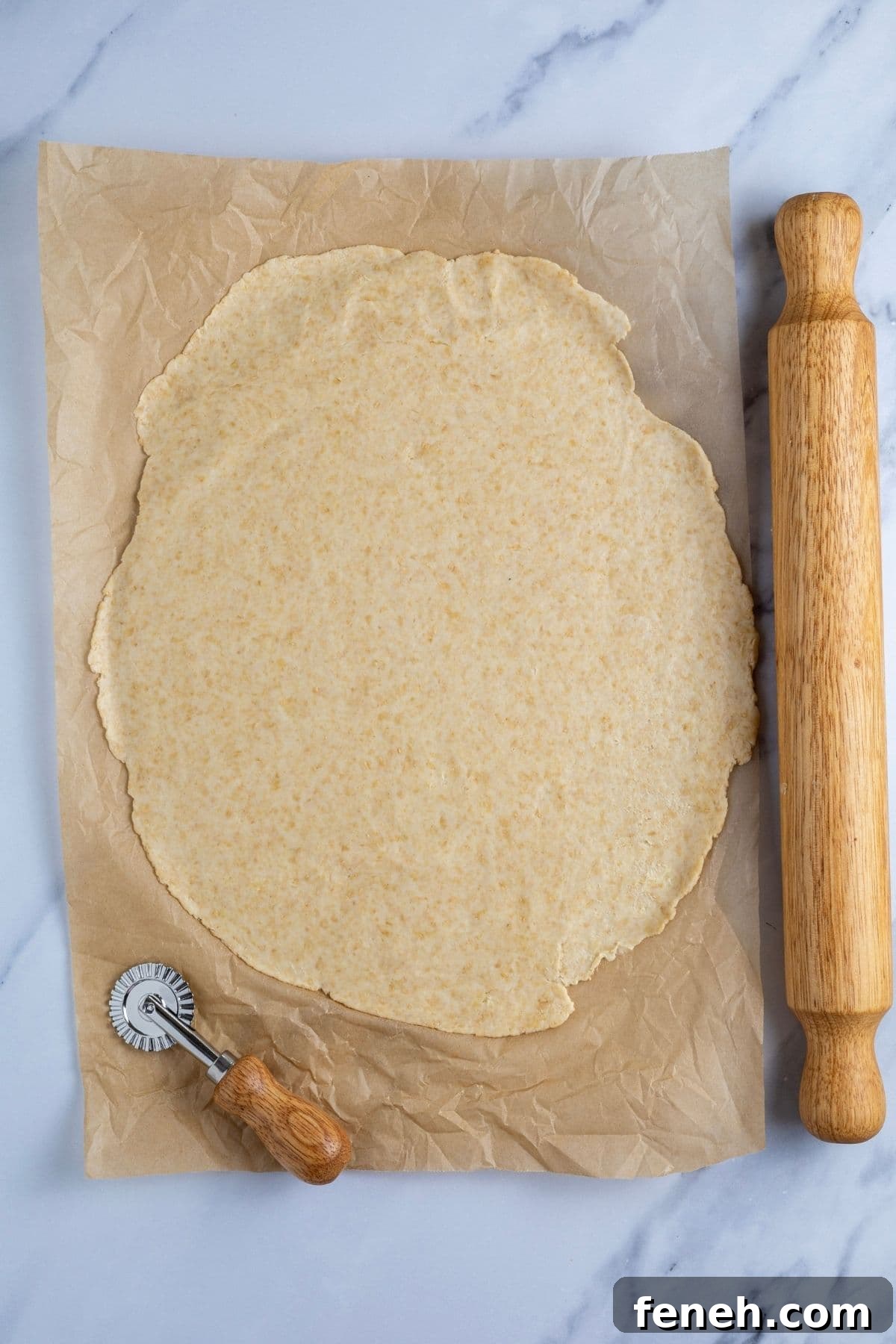 Crispy Whole Wheat Sourdough Crackers Recipe 7 A sheet of whole wheat sourdough cracker dough rolled out really thin on a piece of parchment paper. There is a rolling pin and a small ravioli cutter in the photo too.