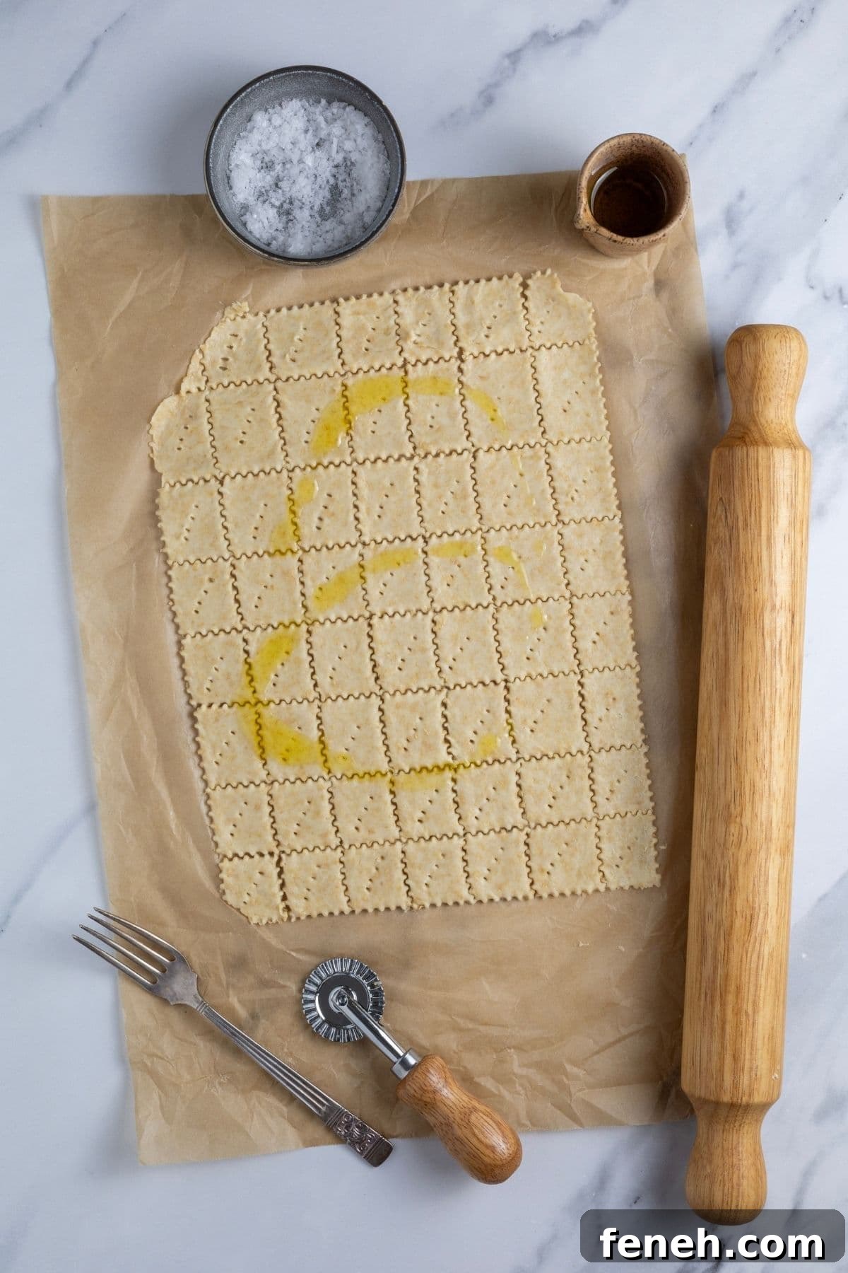 Crispy Whole Wheat Sourdough Crackers Recipe 8 Whole wheat sourdough cracker dough cut into squares and drizzled with olive oil. There is a vintage fork, ravioli cutter, rolling pin, small dish of salt and rolling pin surrounding the cut crackers.