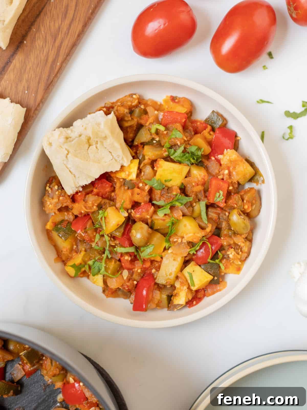 Bowl of thick homemade ratatouille in white bowl with rustic piece of bread.