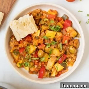 Thick Classic Ratatouille dished up in bowl topped with basil and served with crusty bread on the side.