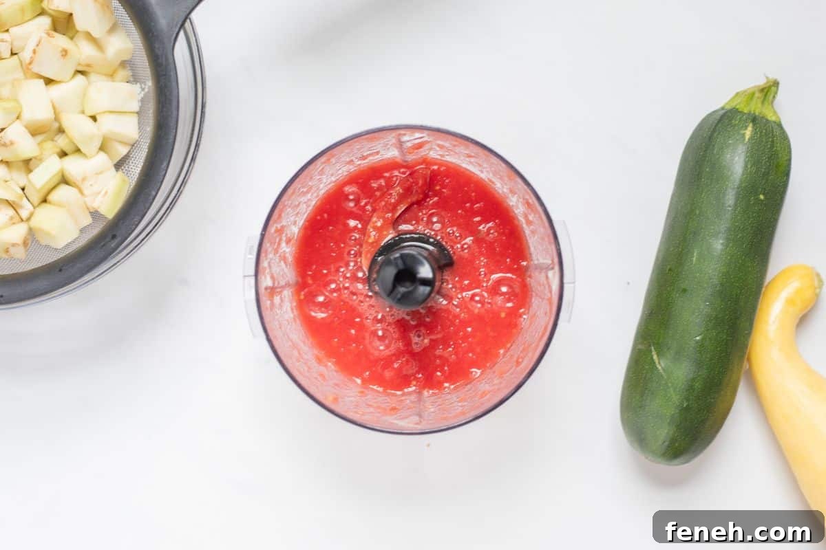 Pureed fresh tomatoes in small food processor next to summer squash.