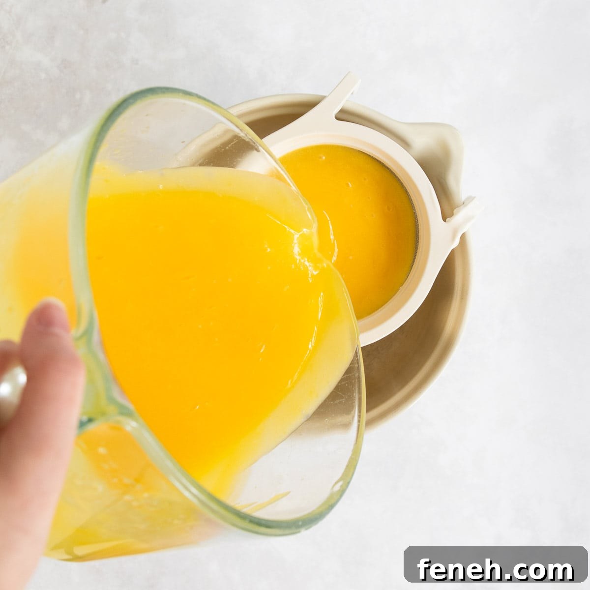 The lemon curd being poured through a fine mesh sieve into a large ceramic jug.