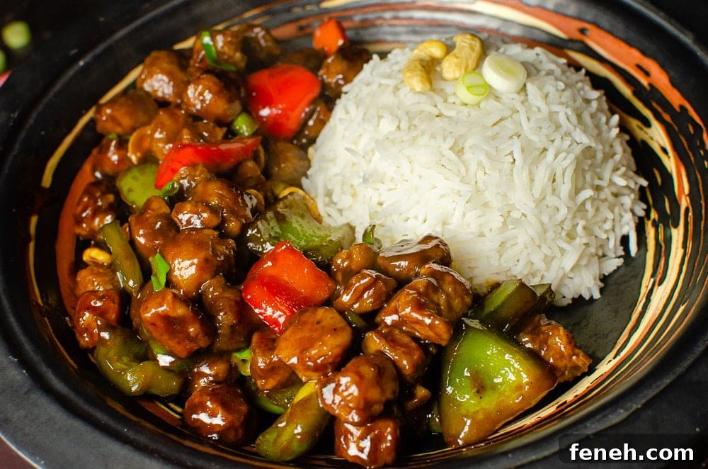 Vegan Kung Pao with red and green peppers served with white rice in a black bowl ready to be eaten