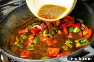 Vegan Kung Pao sauce being added to the red and green peppers in a cast iron dish
