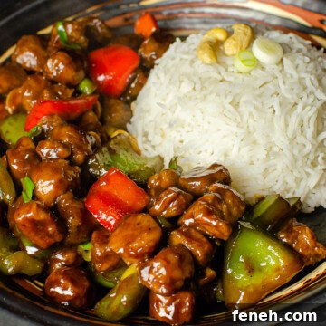 Vegan Kung Pao with red and green peppers served with white rice in a black bowl ready to be eaten