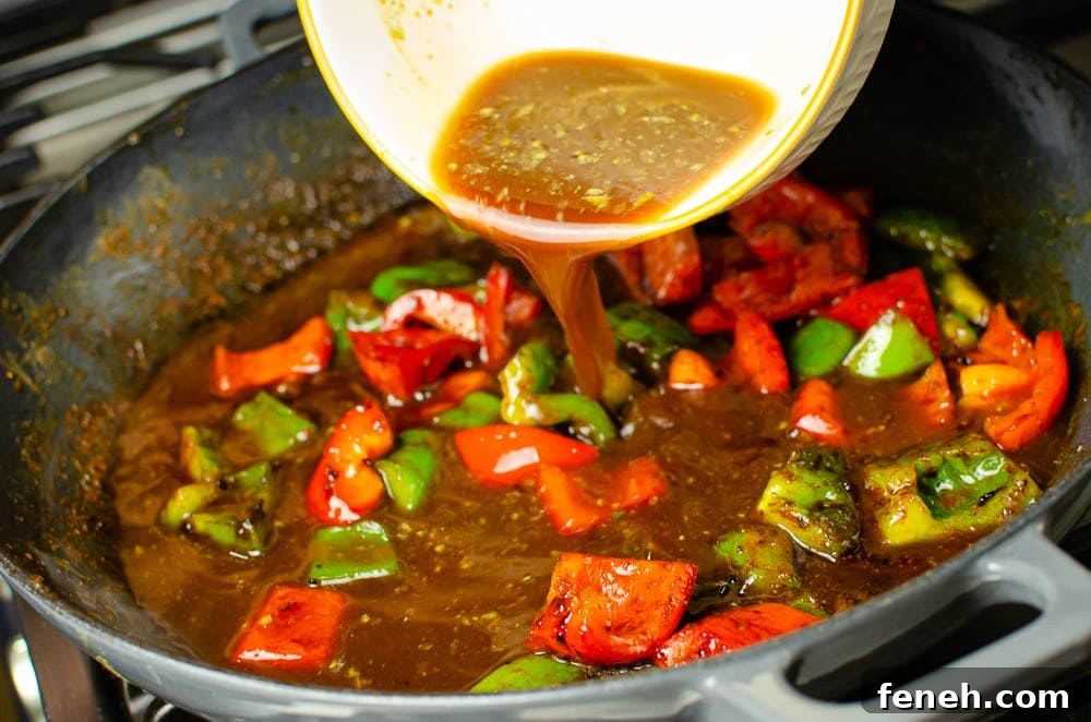 Vegan Kung Pao sauce being added to the red and green peppers in a cast iron dish 