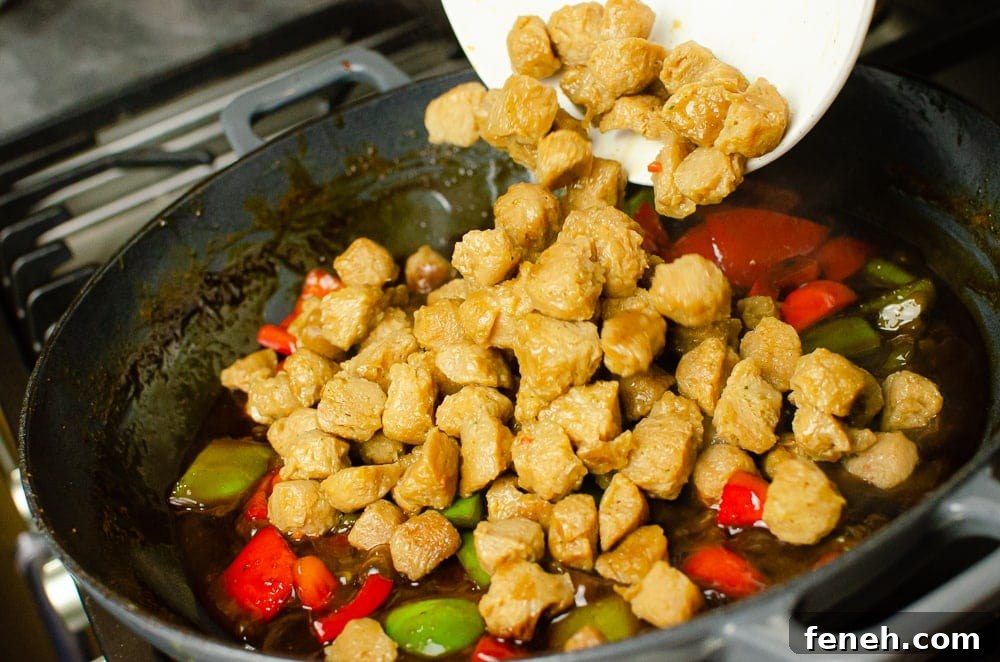 Textured Vegetable Protein being added to the vegan kung pao sauce with red and green peppers