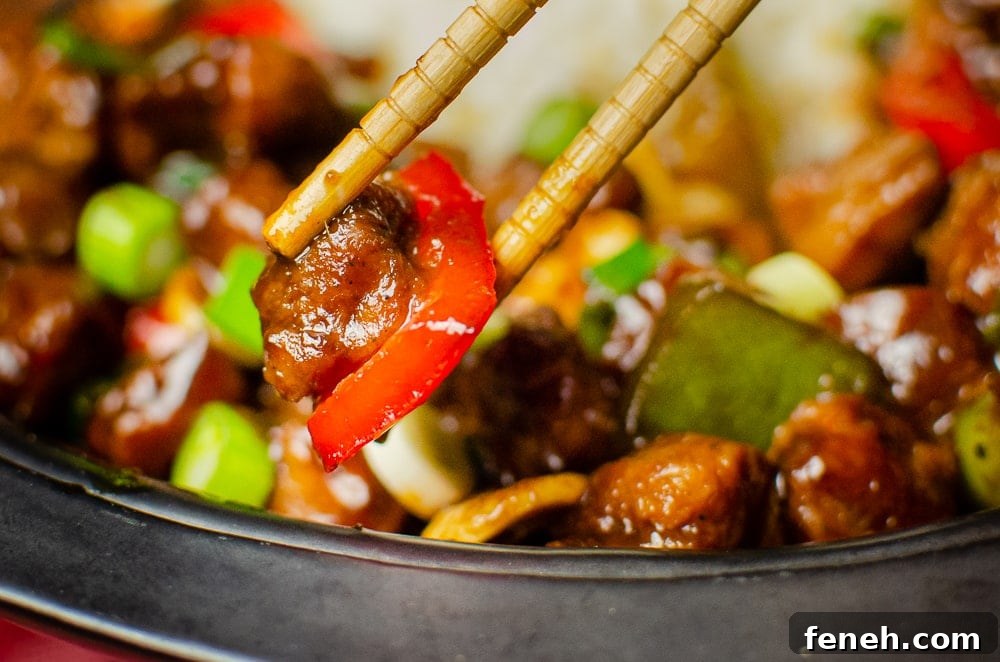 Serving of Vegan Kung Pao, with chopsticks holding a textured vegetable protein chunk and red pepper.