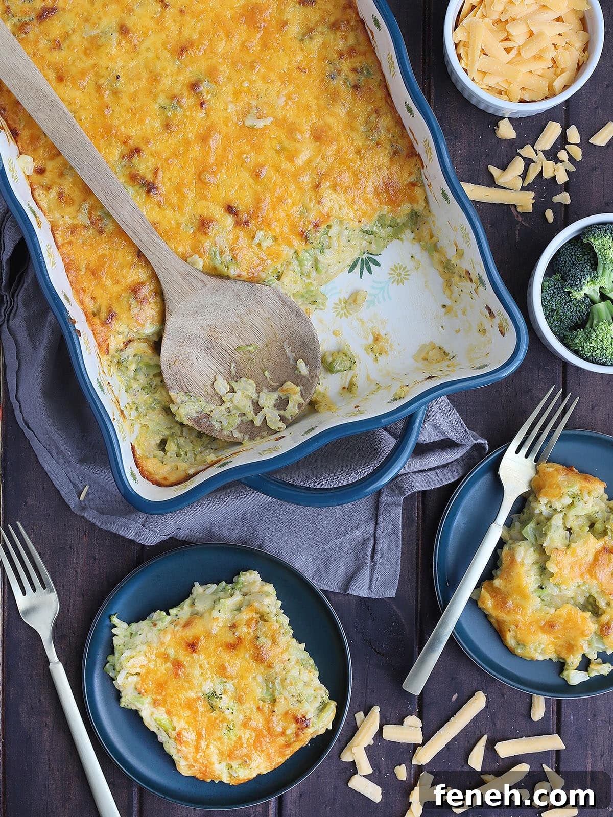 wooden serving spoon laid across the casserole dish with servings of cheesy broccoli casserole on the side