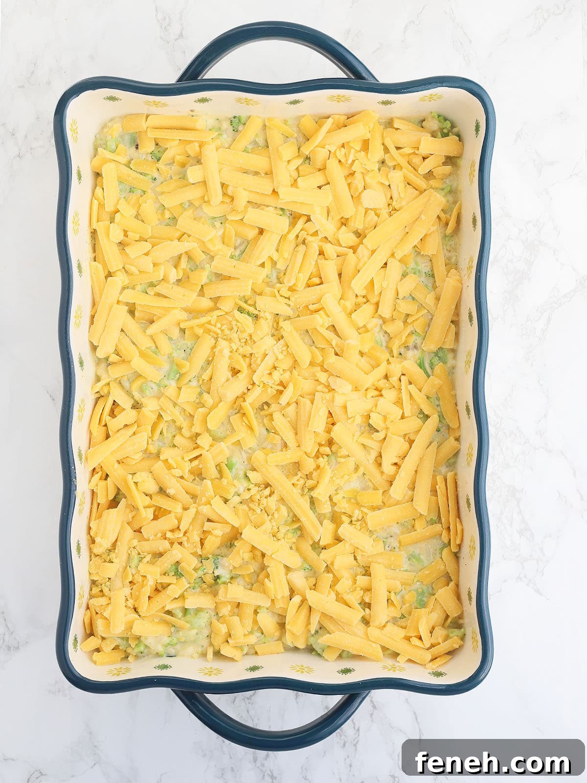 unbaked cheesy broccoli casserole topped with shredded cheese