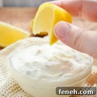 A small dish of tartar sauce, being topped with a squeeze of lemon.