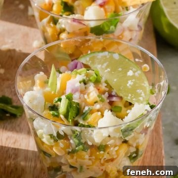 elote in small plastic cups garnished with lime wedges and tortilla chips on wood cutting board.