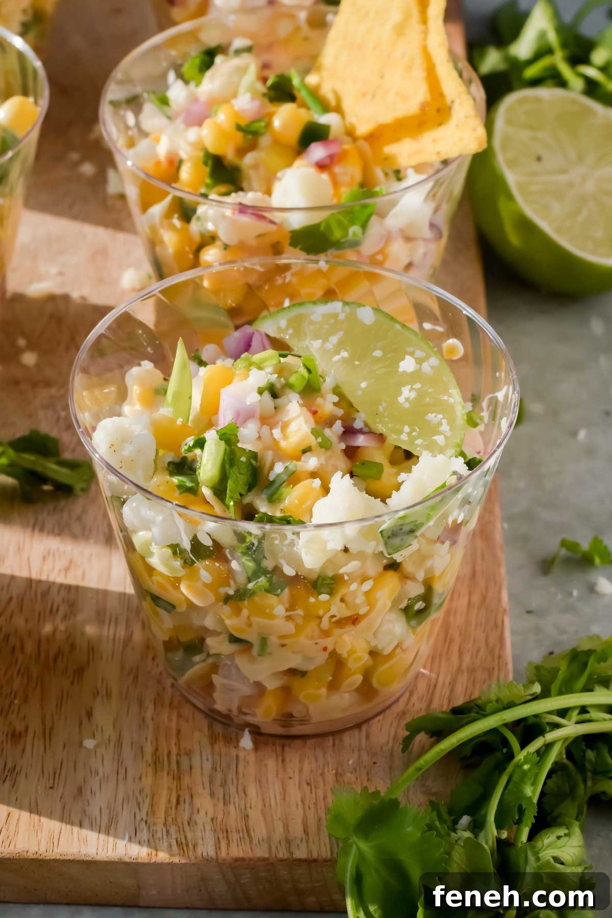 elote in a small glass cup with a lime wedge on top.