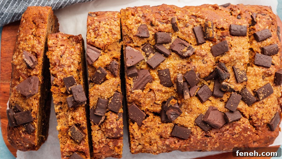 A loaf of gluten-free vegan banana bread topped with chocolate chunks that has been partially sliced.