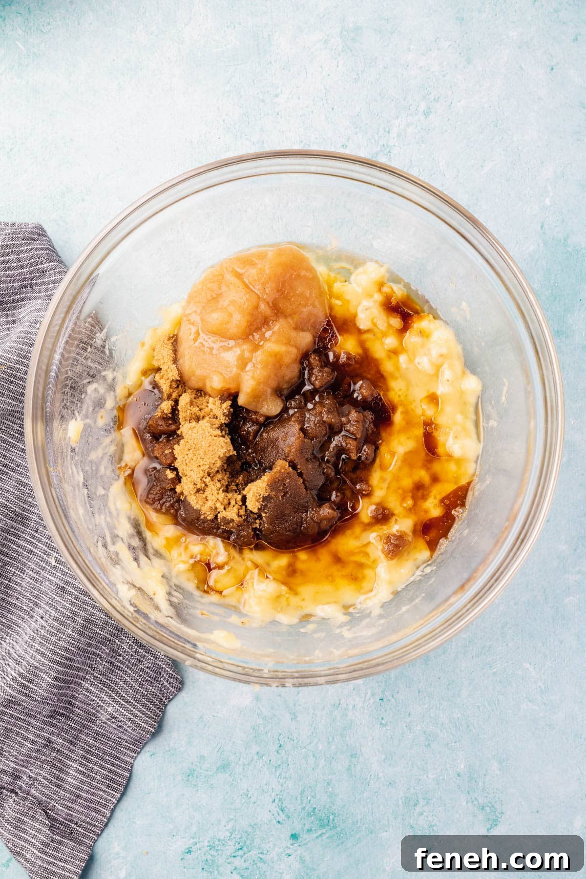 A glass mixing bowl with mashed banana and wet ingredients.