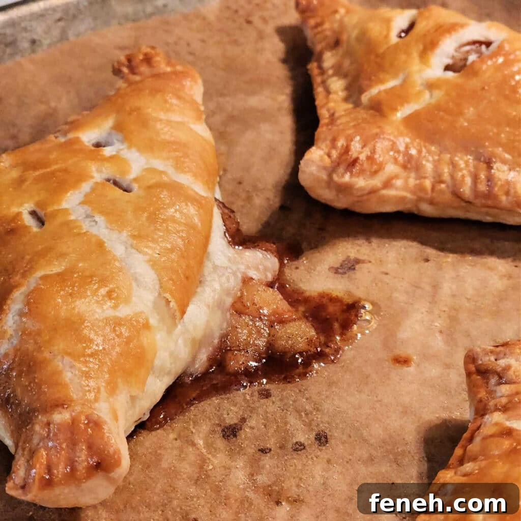 A close up of an apple turnover fresh from the oven. Some of the filling has broken through the crust in the back of the turnover.