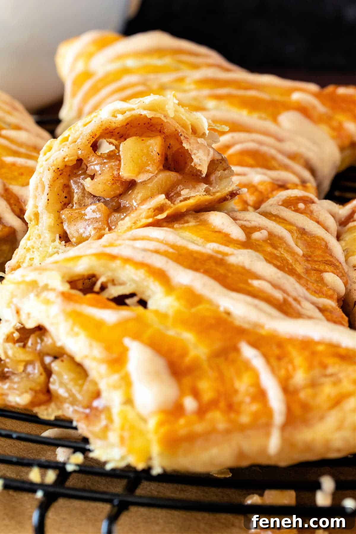 A vertical image of apple turnovers with lines of glaze on them. One is cut open to reveal little chunks of apple.